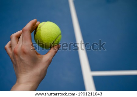 Close-up of tennis ball in hand. Blue hard court with white stripe.