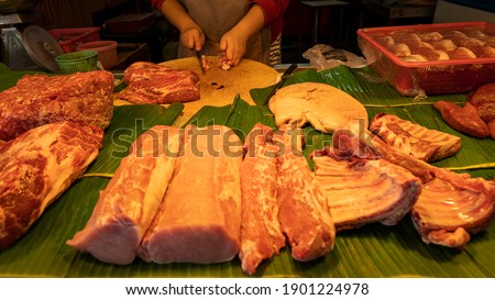 Lots of pork on the table covered with banana leaves and the vendors were cutting them.