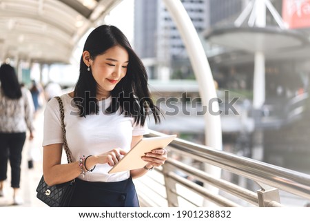 Young adult business working asian woman using digital tablet for online application stock market.  Lifestyle with modern technology. Background with copy space on day. Royalty-Free Stock Photo #1901238832