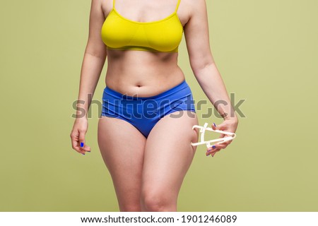 Woman measuring her body fat with caliper on light green background, body care concept