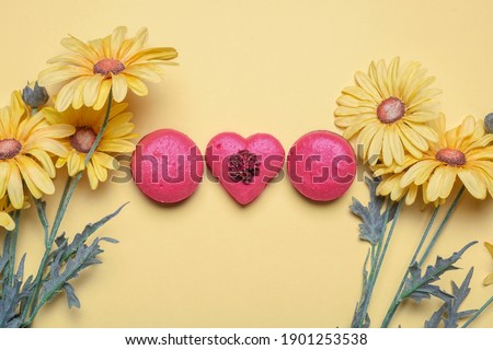 Three red macarons with one heart shaped on a yellow background with spring yellow daisy flowers with copy space and room for text