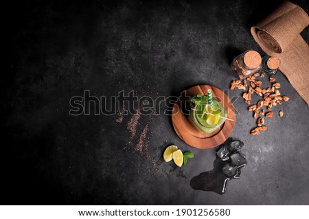 Top view healthy green smoothie in jar glass with walnuts lime ice peppermint poppy seeds on wooden board dark gray background