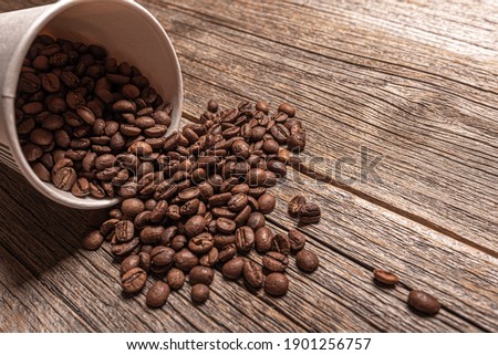 Paper cup with coffee beans on a wooden table.