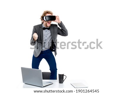 Portrait of curly-haired elegant businessman in vr glasses with hand in fist on chair at table with gadgets