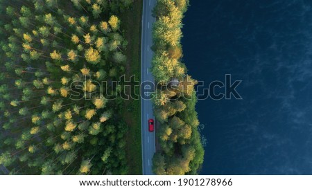 Aerial view of lake, forest and road at misty morning. Red car driving through the forest at sunrise. Highway through deep forest. Royalty-Free Stock Photo #1901278966