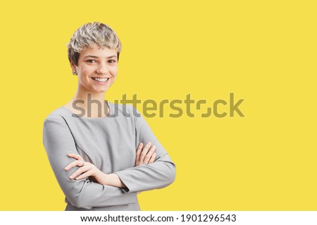 Waist up portrait of confident short-haired woman smiling at camera while standing with arms crossed against pop yellow background, copy space