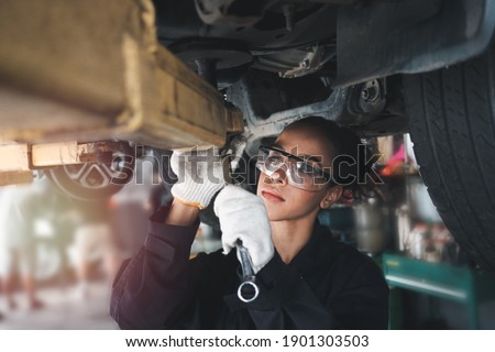 Female auto mechanic work in garage, car service technician woman check and repair customer car at automobile service center, inspecting car under body and suspension system, vehicle repair  shop. Royalty-Free Stock Photo #1901303503
