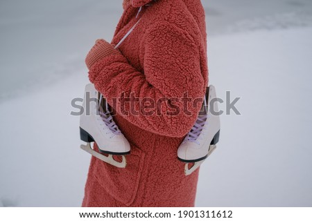 a young woman in a pink eco-fur coat holds white skates on her shoulder. part of the body without a face. winter ice skating concept