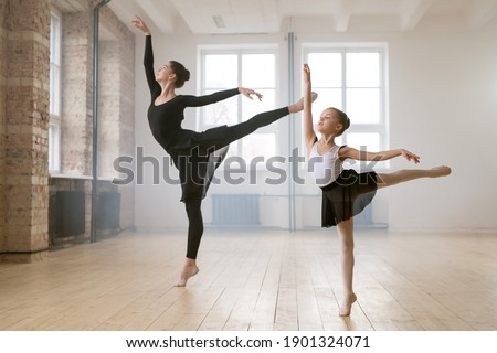 Young woman and little girl standing together in the same ballet pose and dancing in dance studio Royalty-Free Stock Photo #1901324071