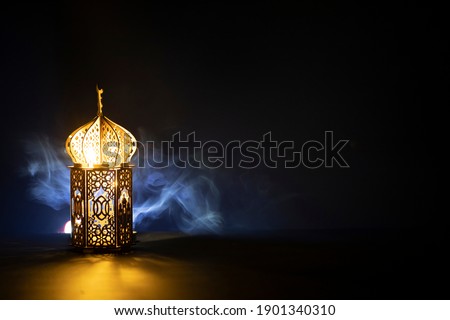 Ornamental Arabic lantern with burning candle glowing at night and glittering golden bokeh lights. Festive greeting card for Muslim holy month Ramadan Kareem. Royalty-Free Stock Photo #1901340310
