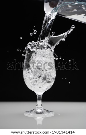 Glass and splashing water on black background