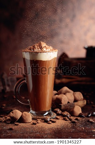 Glass of hot chocolate with whipped cream and truffles on an old brown table. Sweets and drink sprinkled with cocoa powder.