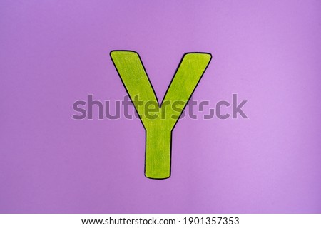 Uppercase letter Y colored in green by pencil top view on pink background.