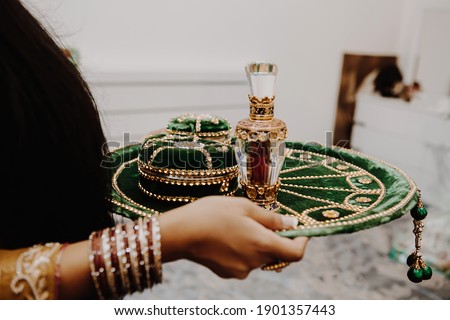 Female hands with round golden emerald green velvet indian tray - mehndi wedding plate with henna in box and perfume bottle close up Royalty-Free Stock Photo #1901357443