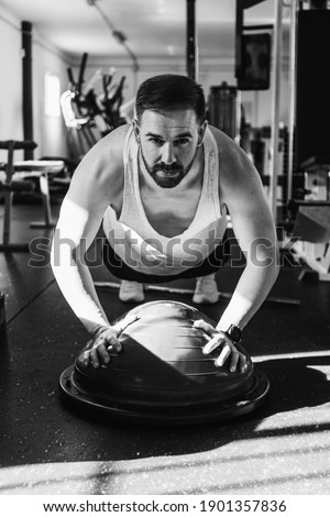 Man exercising on bosu ball in gym in black and white. Health and wellness concept. Sport.