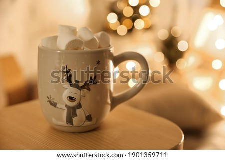 Cup of hot drink with marshmallows on small wooden table, space for text. Christmas atmosphere