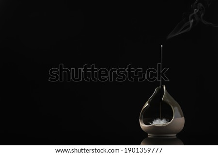 Incense stick smoldering in holder with lotus flower on black background. Space for text Royalty-Free Stock Photo #1901359777