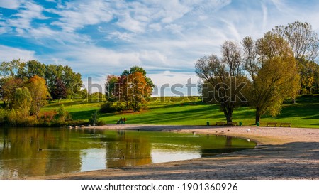 Autumn landscape at lake, trees, green grass, blue sky clouds in background 
