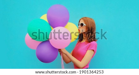 Portrait of beautiful young woman with bunch of colorful balloons blowing her lips sending sweet air kiss on a blue background