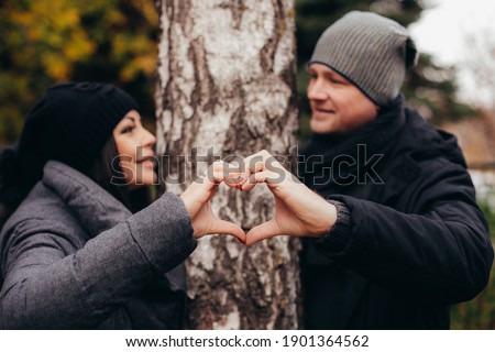 A young couple of lovers makes a heart out of hands against a tree in the autumn forest on Valentine's Day. High quality photo