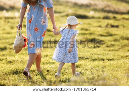 Young mother walking with her little daughter in the green field. Family holiday in garden. Portrait mom with child together on nature. Mum, little daughter outdoors. Happy Mothers Day. Close up.