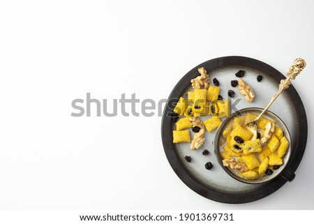 raisins and walnuts on a table next to cornflakes with milk in a cup, on a white background