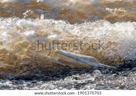 A message in a clear bottle washing ashore in a golden wave. Sunny day. Foam and lots of detail. Bottle on its side.