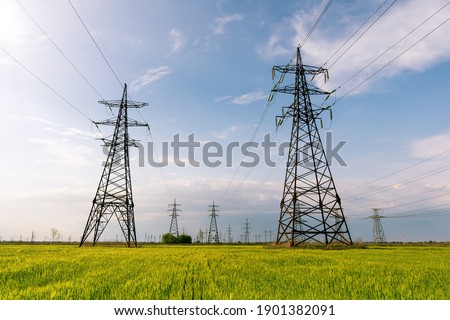 High voltage power lines leading through a green field. Transmission of electricity by means of supports through agricultural areas. Royalty-Free Stock Photo #1901382091
