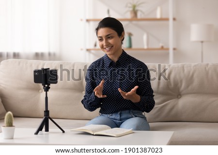 Indian female popular video blogger shoot video content at home make topical review before webcam of phone fixed on tripod. Young hindu lady coach talk on camera of cell device broadcast speech online Royalty-Free Stock Photo #1901387023