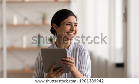 Full of dreams. Smiling mixed race lady web shop customer hold pad pc look aside choose goods plan purchases. Positive indian female relax at home with digital tablet enjoy modern device possibilities Royalty-Free Stock Photo #1901389942