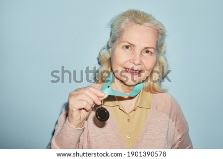 Portrait of smiling senior woman wearing medal and looking at camera while standing against blue background, copy space