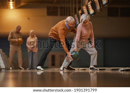 Wide angle side view at modern senior couple playing bowling together while enjoying active entertainment at bowling alley, copy space