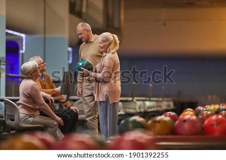 Wide angle side view at group of senior people playing bowling together while enjoying active entertainment at bowling alley, copy space