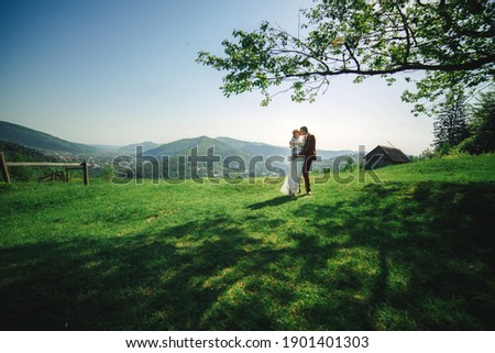 happy stylish bride and groom running and having fun in mountains on summer sunny day. gorgeous newlywed couple laughing, true feelings. emotional romantic moment
