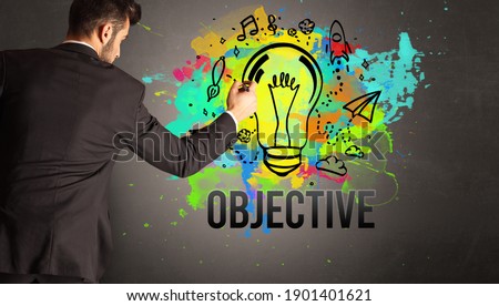 businessman drawing colorful light bulb with OBJECTIVE inscription on textured concrete wall, new business idea concept