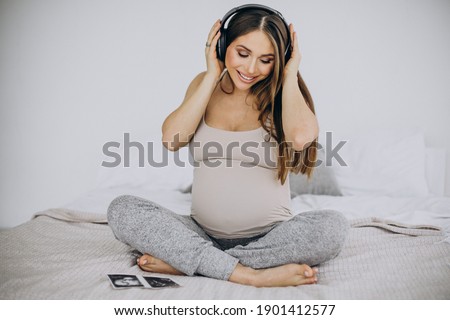 Pregnant woman with ultrasound photo listening to music