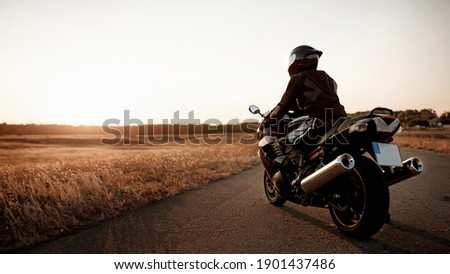 Motorcyclist turned his back in helmet and gear against the backdrop of beautiful sunset light with copy space Royalty-Free Stock Photo #1901437486