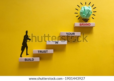 Success business process symbol. Wood blocks stacking as step stair on yellow background, copy space. Businessman icon. Words 'build trust in your brand'. Business and trust brand concept.