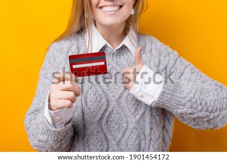 Close up photo of smiling woman holding red credit card and showing thumb up
