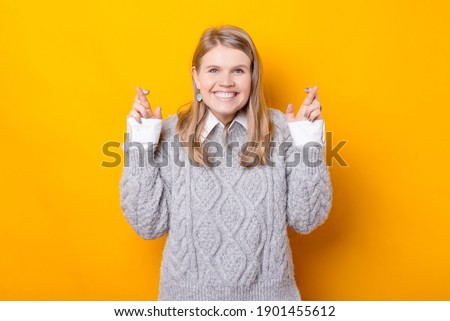Cheerful smiling young woman crossing fingers over yellow background
