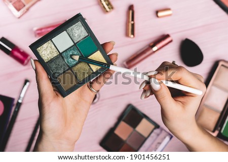 Woman working with green eyeshadow palette on pink flat lay cosmetics collection background. Tools in beauty industry - lipsticks, blush, glosses. . High quality 