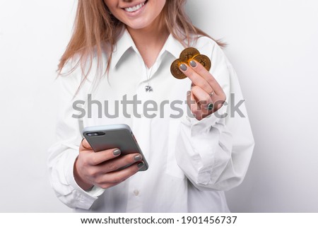 Close up photo of cheerful woman holding smartphone and bitcoins