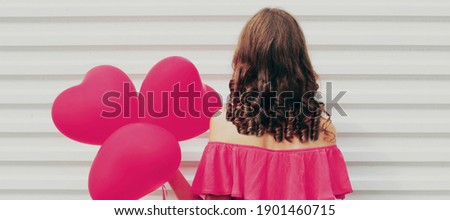 Rear view of woman with pink heart shaped balloon on a white background
