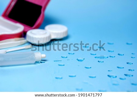 contact lenses, case, and tools on a blue background with water drops