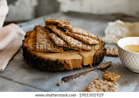 Healthy and nutritious diet bread with sesame and sunflower seeds on a thin crunchy malt base. Near natural bee honey and a wooden stand sawn