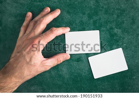 Hand hold blank business card with rounded corners on chalkboard texture, top view
