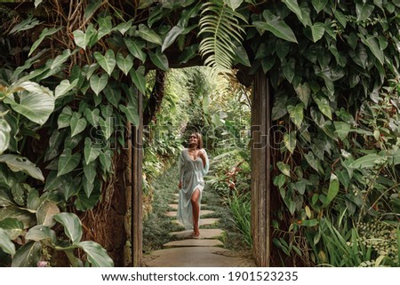 Young woman walking in tropical garden in long summer dress, greenery and palm trees around, enjoying nature Royalty-Free Stock Photo #1901523235