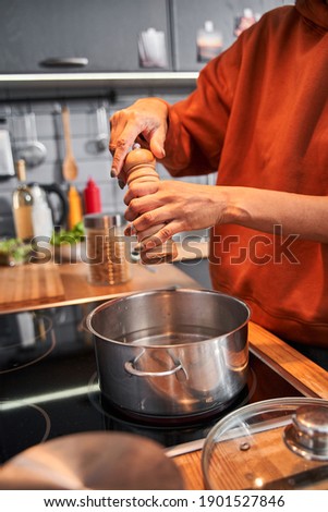 Cropped view of the multiracial woman salt pasta and sprinkle with species while preparing dinner with her best friend at the kitchen. Coolinary concept. Stock photo