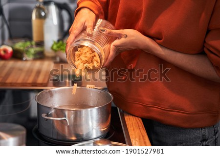 Cropped view of the multiracial woman pouring pasta at the pan while preparing dinner with her best friend at the kitchen. Coolinary concept. Stock photo
