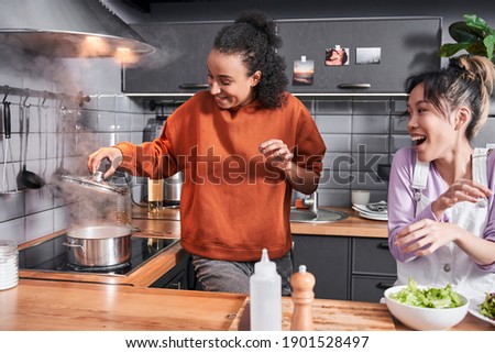 Waist up portrait of the multiracial woman laughing while preparing salad at the table. Girl cooking together at the kitchen. Happy weekend of best friends concept. Stock photo